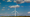 A wind turbine stands in an open field near Arlington, Oregon, with a partly cloudy blue sky above.